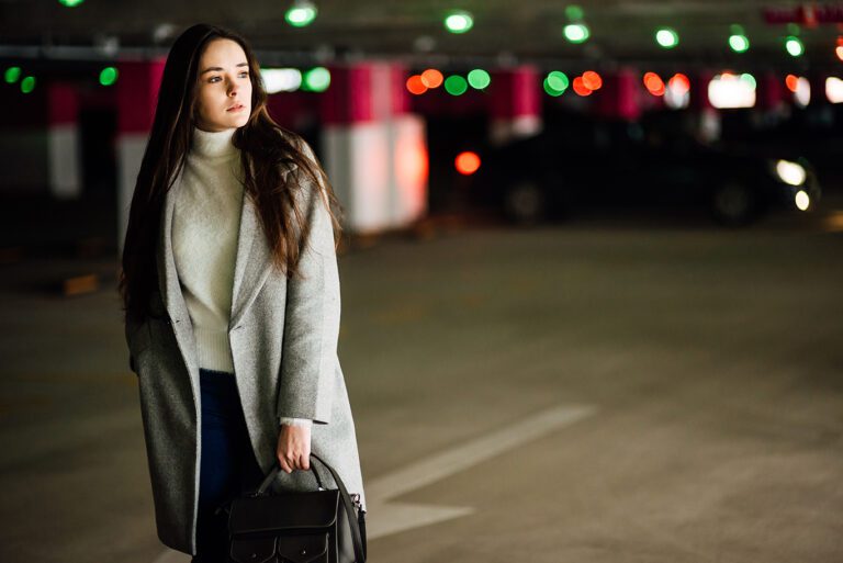 Beautiful young girl in a gray coat and with bag on car parking