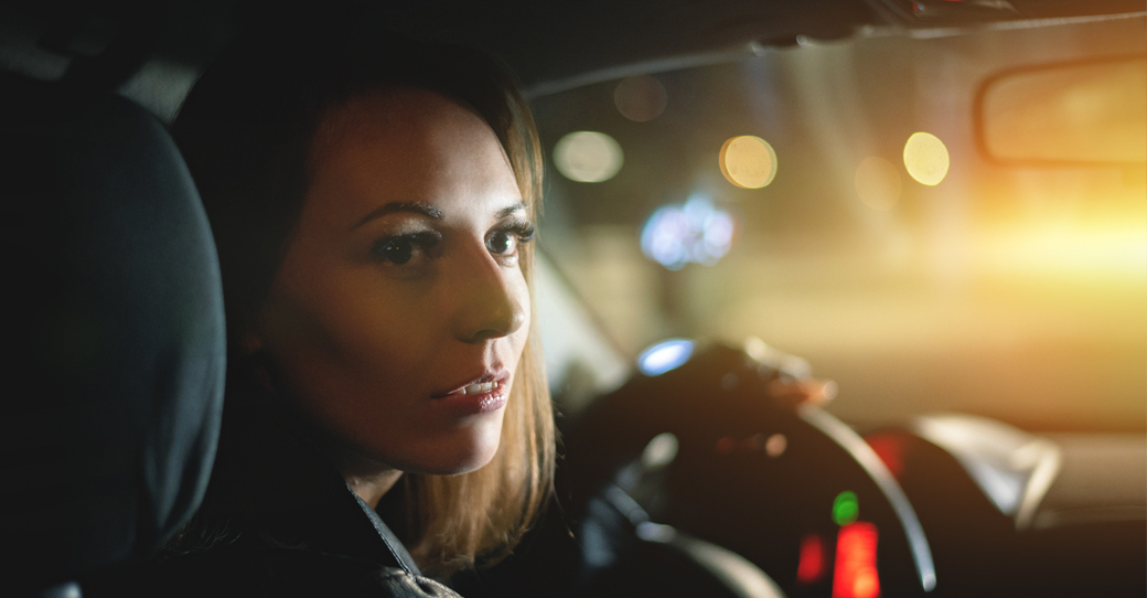 A woman in the driver's seat of her car looks behind her.