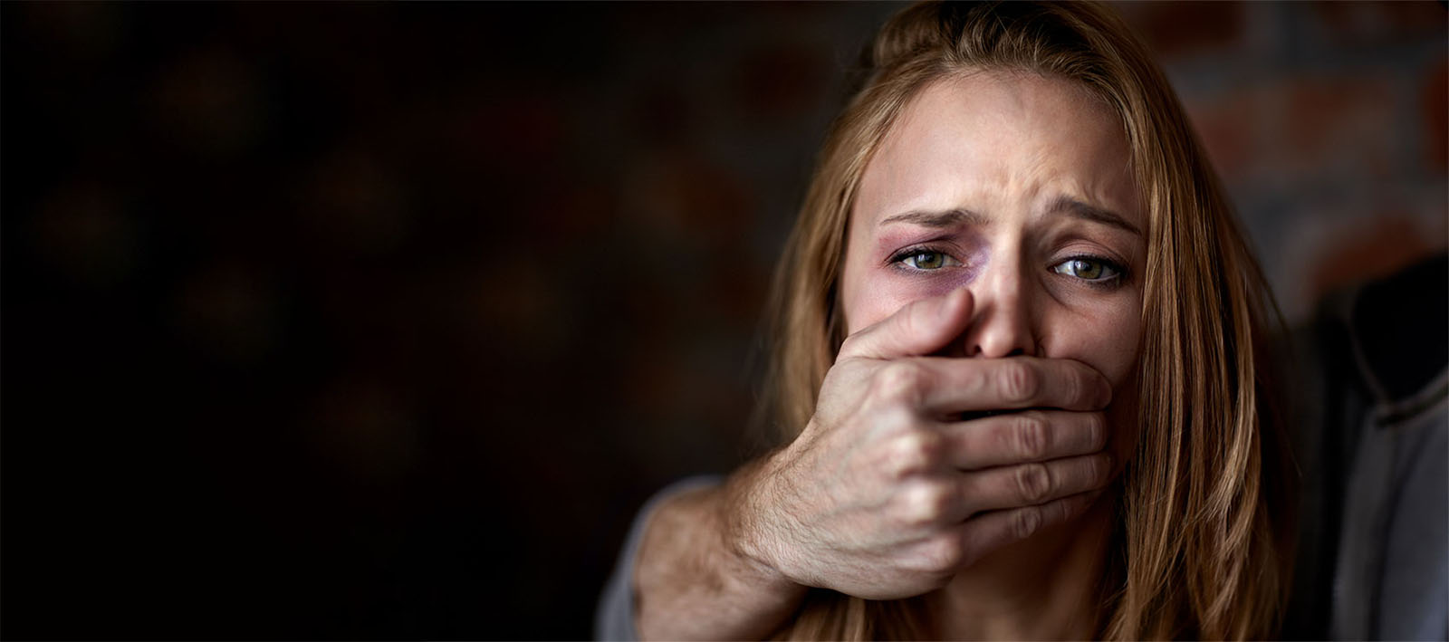 A Woman with a Black Eye being held by a Man, his Hand over her Mouth