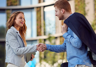 Two people shaking hands in front of a building