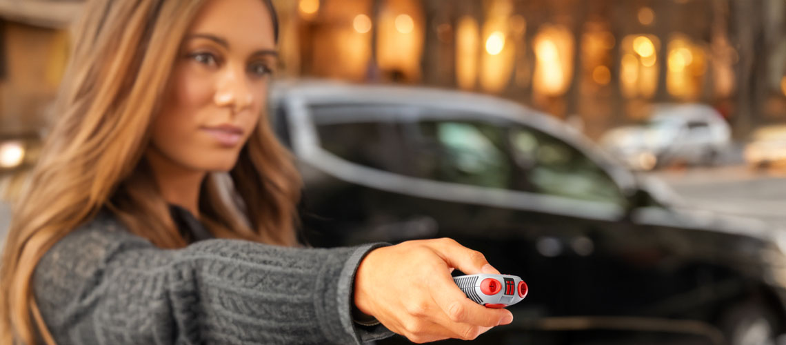 A woman standing near a street aims her AIIRO non-lethal defense tool.